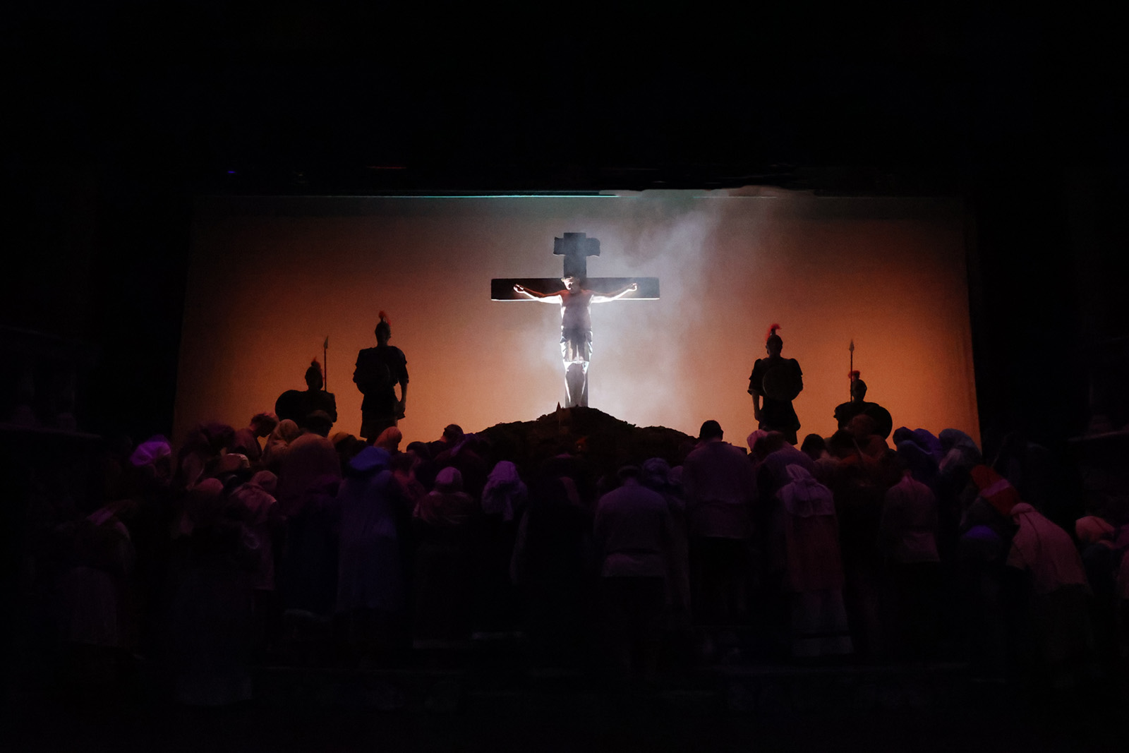 A crowd of people with mournful expressions gather near Jesus on the cross. Some clasp their hands, others lift their hands.